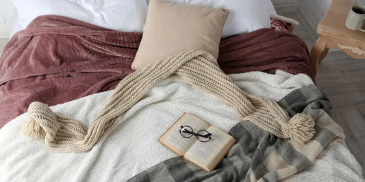 Plaid laine, plaid velours, coussin et livre sur un lit