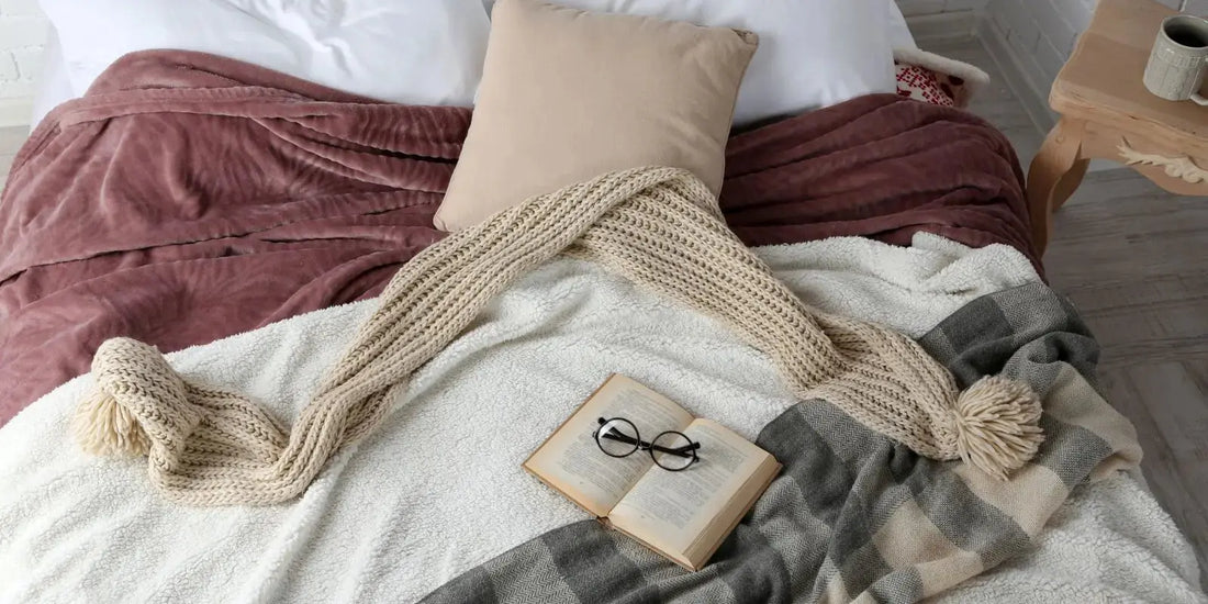 Plaid laine, plaid velours, coussin et livre sur un lit