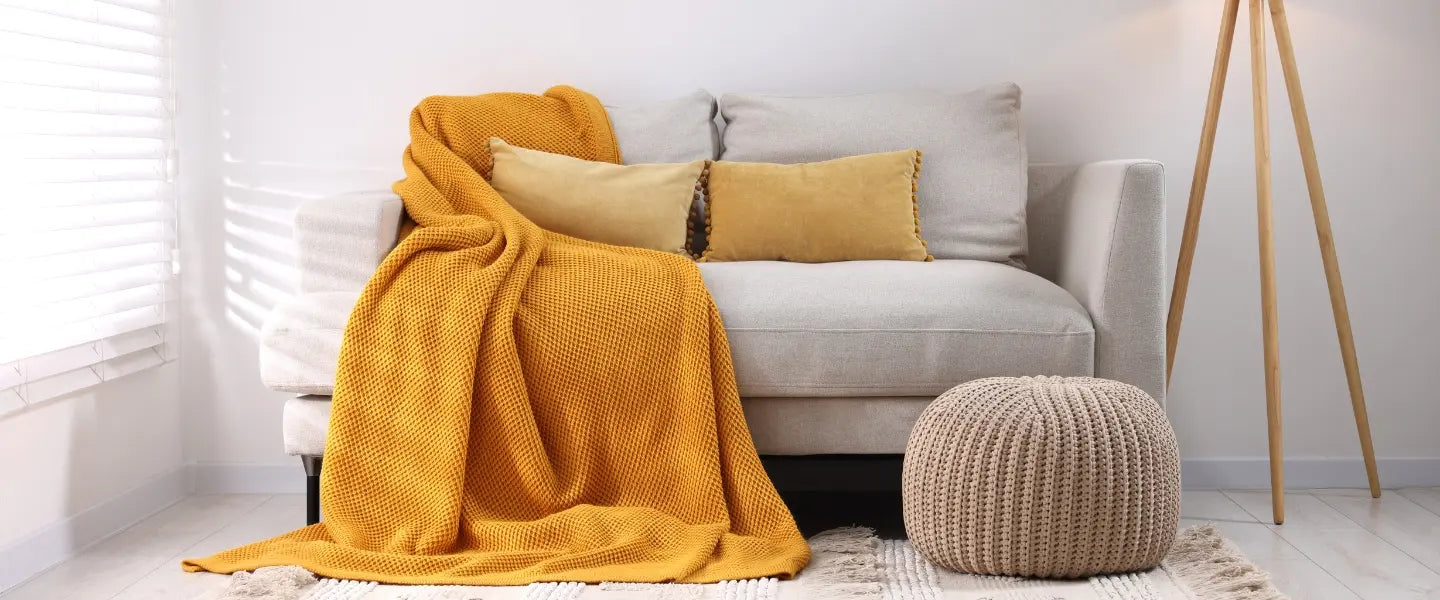 Plaid moutarde disposé sur un canapé gris clair avec deux coussins rectangulaire camaïeux moutarde