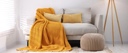 Plaid moutarde disposé sur un canapé gris clair avec deux coussins rectangulaire camaïeux moutarde