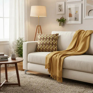 Coussin Kali moka adossé sur un canapé avec plaid dans un salon cosy